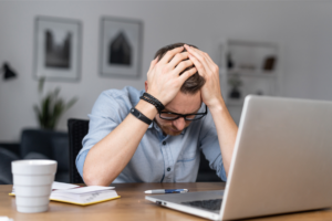 Depressed young businessman holding head in hands, has problem, a laptop on the desk