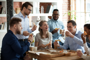 Happy diverse team people talking laughing at funny joke eating ordered pizza in office, friendly employees group enjoy positive emotions sharing lunch together having fun at work break on friday